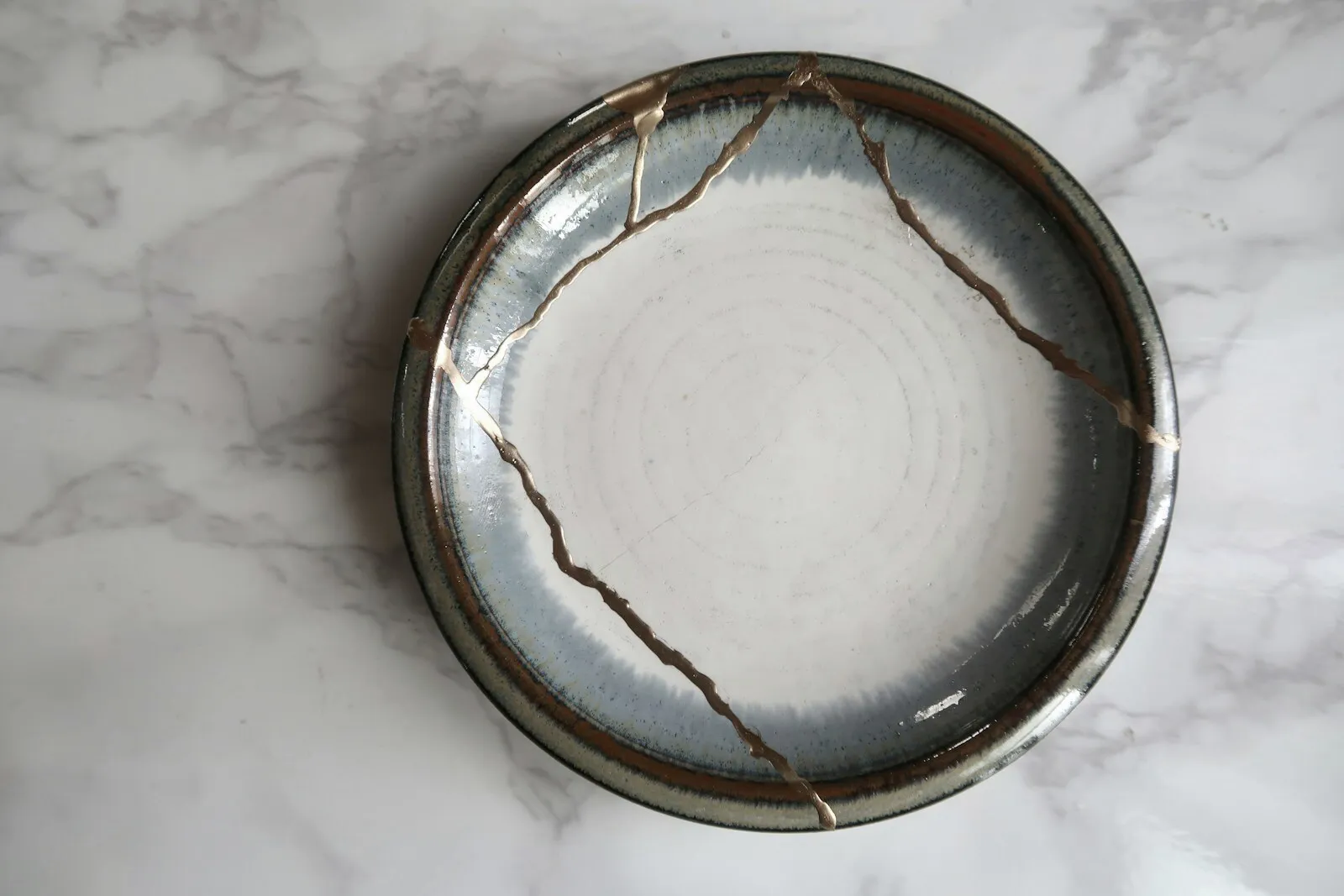 A ceramic bowl mended with gold seams, resting on pale stone
