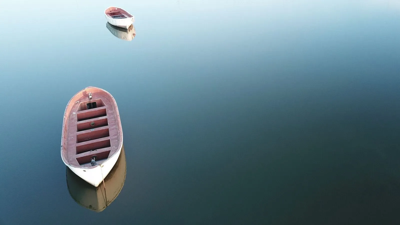 Two small boats at different distances on flat, calm water