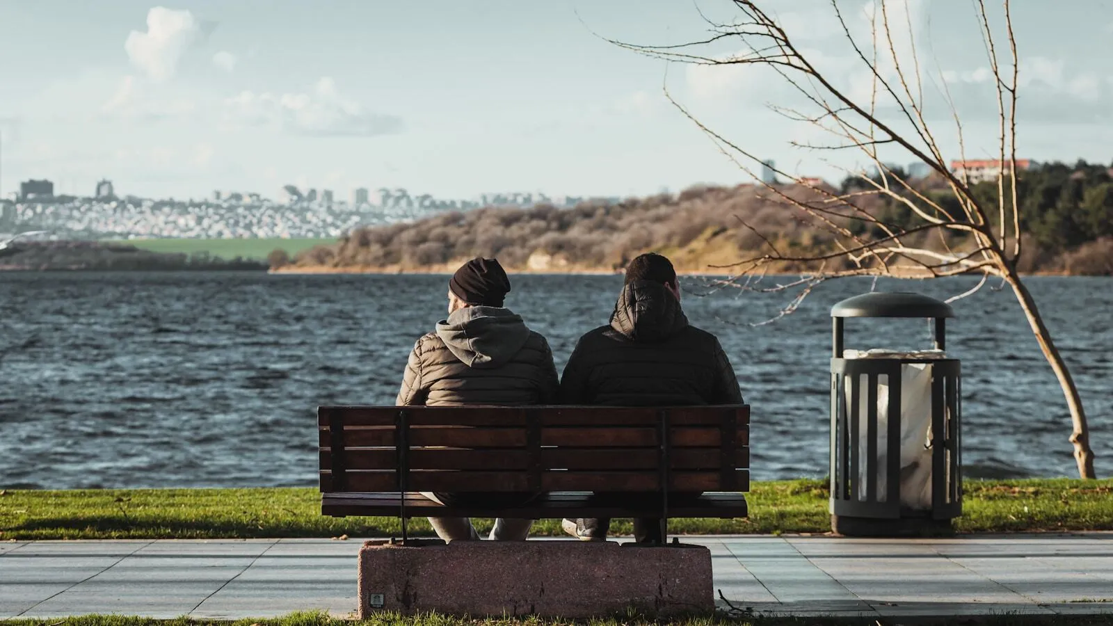 Two people sitting together on a bench, looking out over water