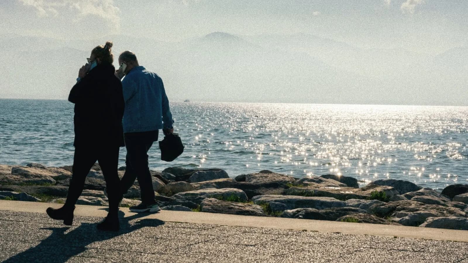 Two people walking a shoreline path beside calm water