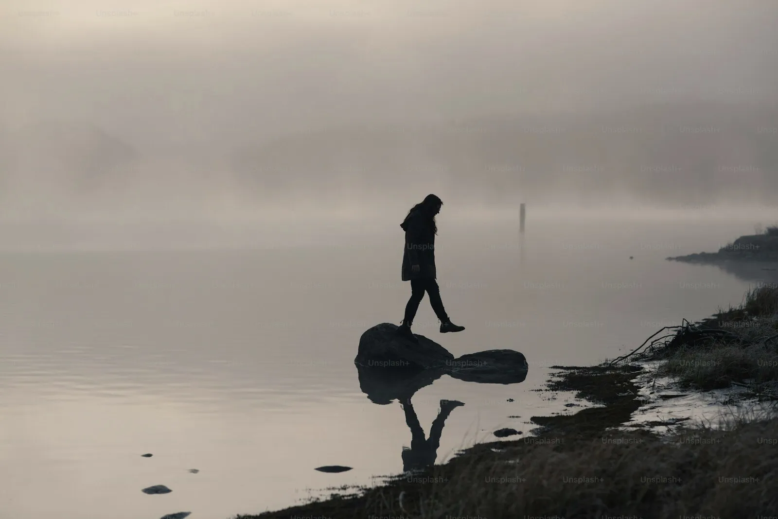 A person walking alone beside still, misty water