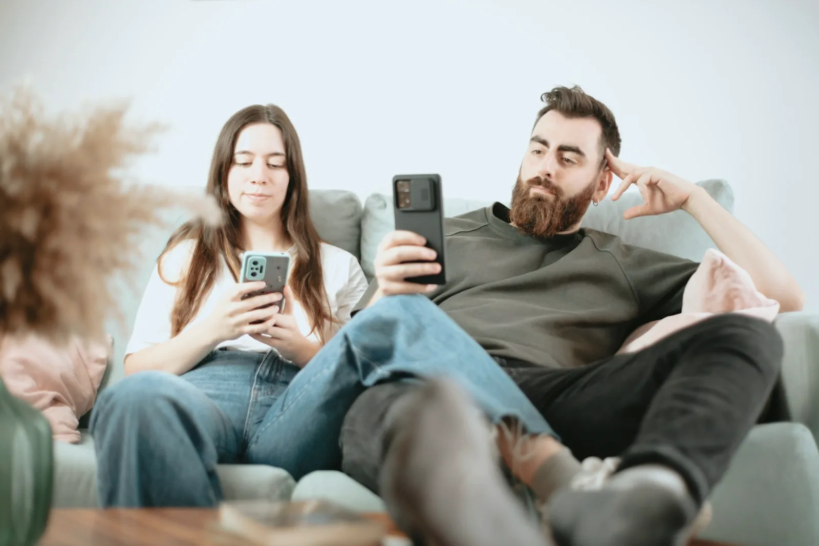 A couple sitting together on a sofa, one absorbed in a phone