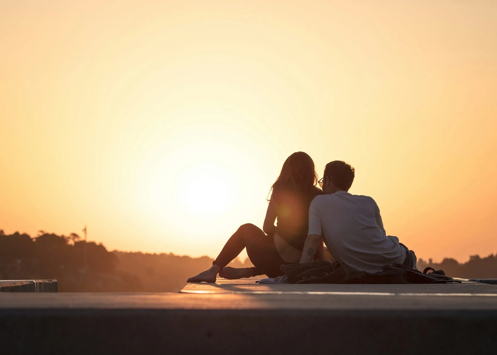 A couple sitting close together outdoors at sunset